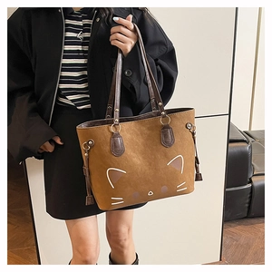 Close-up of brown suede tote bag with minimalist white cat face embroidery and tassel charm