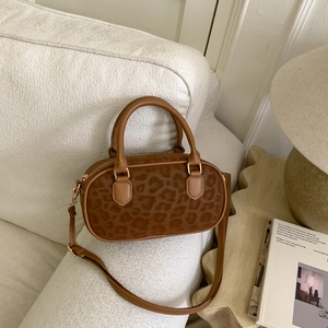 Detail of leopard print bowling bag with gold hardware on a soft white sofa