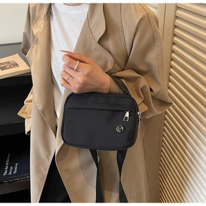 Détail du sac bandoulière en nylon noir porté avec un trench beige pour un style décontracté