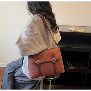 Detail view of a vintage rust red suede messenger bag with dark brown leather buckle straps