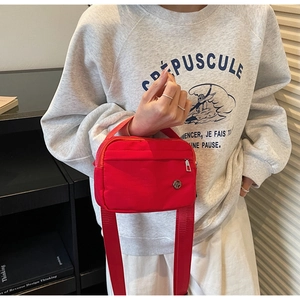 Detailed close-up of a red nylon crossbody bag with wide shoulder strap and metal logo