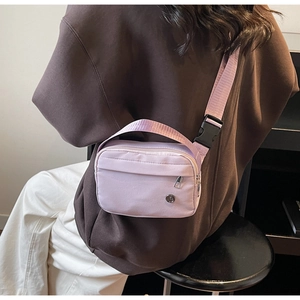 Detail view of a pale purple nylon crossbody bag worn by a model in a minimal indoor setting
