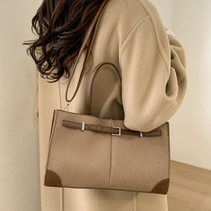 Detail of a brown woven pattern handbag featuring leather trim and silver metal buckle