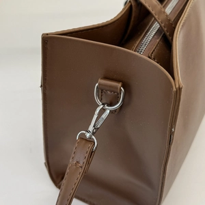 Detail of silver D-ring and lobster clasp on dark brown synthetic leather bag side