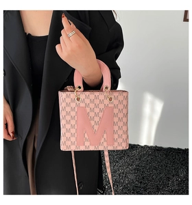 Detail of pink handbag featuring embossed M logo and gold metal hardware accents
