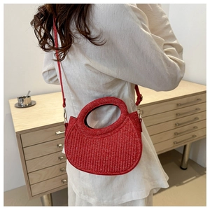 Detail of a red woven crescent bag with a unique circular handle and slim crossbody strap