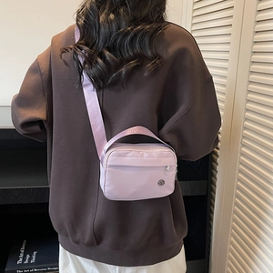 Minimalist lavender nylon crossbody bag with adjustable strap worn on brown oversized hoodie