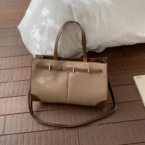 Chic brown woven tote bag with leather accents and adjustable shoulder strap on wood floor