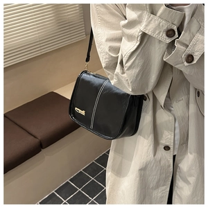 Détail d'un sac bandoulière en cuir noir avec surpiqûres blanches et logo doré chic