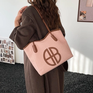Pink woven tote bag with AB logo patch and brown leather straps on a wool coat model