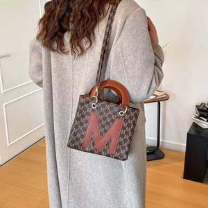 Chic brown monogram satchel bag with leather handles shown on a model in a gray wool coat