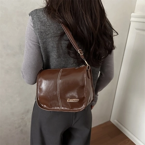 Retro dark brown crossbody shoulder bag with glossy finish and metal logo on a model