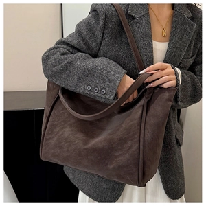 Close-up of a large dark brown suede tote bag worn on shoulder with a stylish grey blazer