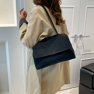 Grand sac à bandoulière noir mat minimaliste porté avec un trench-coat kaki élégant