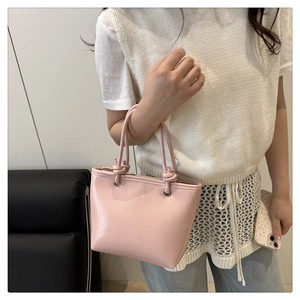 Close-up of pink glossy underarm bag with knot detail and sleek minimalist design