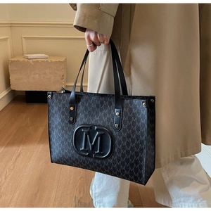 Detail shot of black monogram tote bag with M logo, styled with a beige trench coat