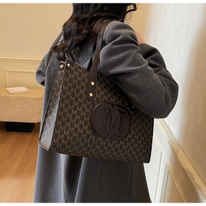 Detail of large brown M-print tote bag worn on shoulder with grey tweed coat