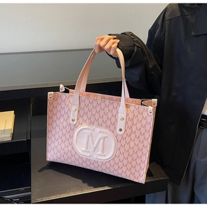 Detail of pink tote bag with M-pattern print and large embossed logo carried by model