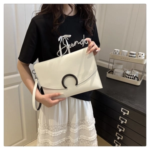 Close-up of a white envelope clutch bag with black crescent buckle and wrist strap detail