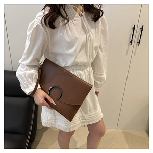 Detail of a brown wristlet clutch featuring a large black semi-circular decorative metal buckle