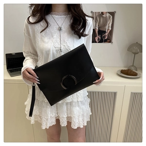 Detail of a black matte leather clutch featuring a stylish dark grey crescent metal buckle