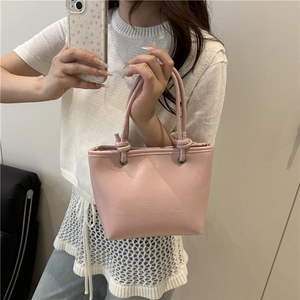 Pink minimalist leather tote bag with stylish knot handle detail shown in lifestyle setting