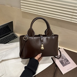 Detail of dark brown patent leather handbag with golden gourd pendant and smooth texture