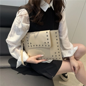 Minimalist beige leather clutch bag with silver square rivets shown in lifestyle setting