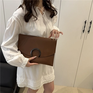 Minimalist dark brown envelope clutch bag with metal buckle shown in a lifestyle setting