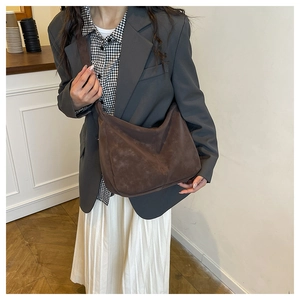 Close-up of a large dark brown suede Hobo bag worn by a model in a minimalist setting
