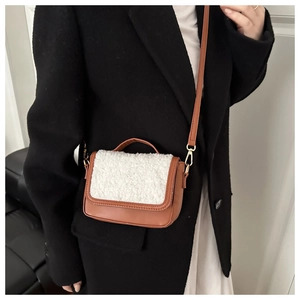 Detailed look at brown leather crossbody bag with white faux fur flap on black coat