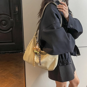 Sac hobo beige minimaliste avec pendentif ours porté par un mannequin dans un salon moderne