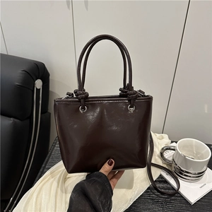 Deep brown glossy trapezoid handbag with decorative knot handles and slim shoulder strap