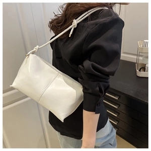 Close-up of minimalist white shoulder bag featuring decorative knots and textured stitching
