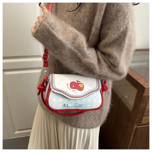 Detail shot of a mini plaid crossbody bag with apple embroidery and a blue bow accent
