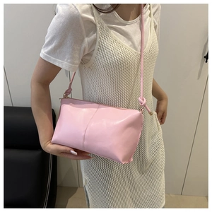 Side view of a minimalist pink leather crossbody bag worn by a model with knot detail