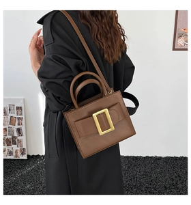 Close-up of brown leather bag featuring an elegant gold buckle and shoulder strap