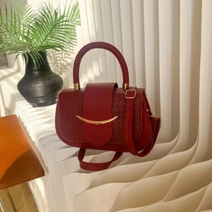Deep red saddle bag with woven texture and gold crescent hardware in a chic indoor setting