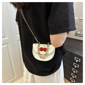 Detail of white saddle bag with red cherry accents and gold chains worn as a crossbody