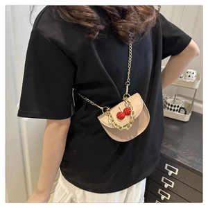 Detail of beige saddle bag featuring red cherry charm and gold chunky chain strap