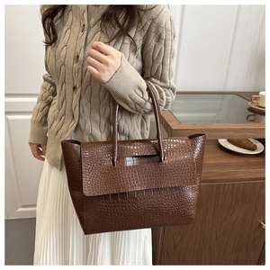 Model wearing a dark brown crocodile pattern tote bag with beige knit sweater and white skirt