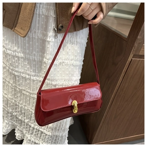 Detail of deep red patent leather shoulder bag with a polished golden U-shaped clasp