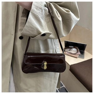 Detail of a dark brown patent leather baguette bag with a gold buckle worn by a model