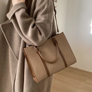 Detailed close-up of brown woven tote bag featuring leather handles and adjustable strap