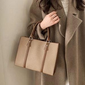 Close-up of a woven texture tote bag with brown leather trim held by a model