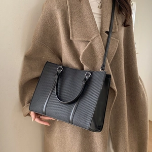 Retro black tote bag with textured panels and crossbody strap on camel coat model
