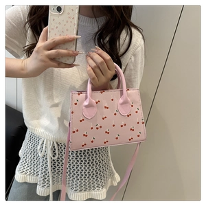 Dettaglio mini borsa a mano rosa con stampa ciliegie mostrata dal modello, borsa a bauletto