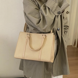 Detail of woven tote bag with leather trim worn with a dark green trench coat