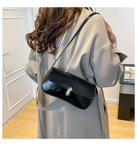 Detail of black glossy patent leather shoulder bag featuring a golden twist lock closure