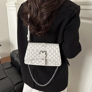 Petit sac carré blanc à motif M avec bandoulière chaîne porté sur un costume noir